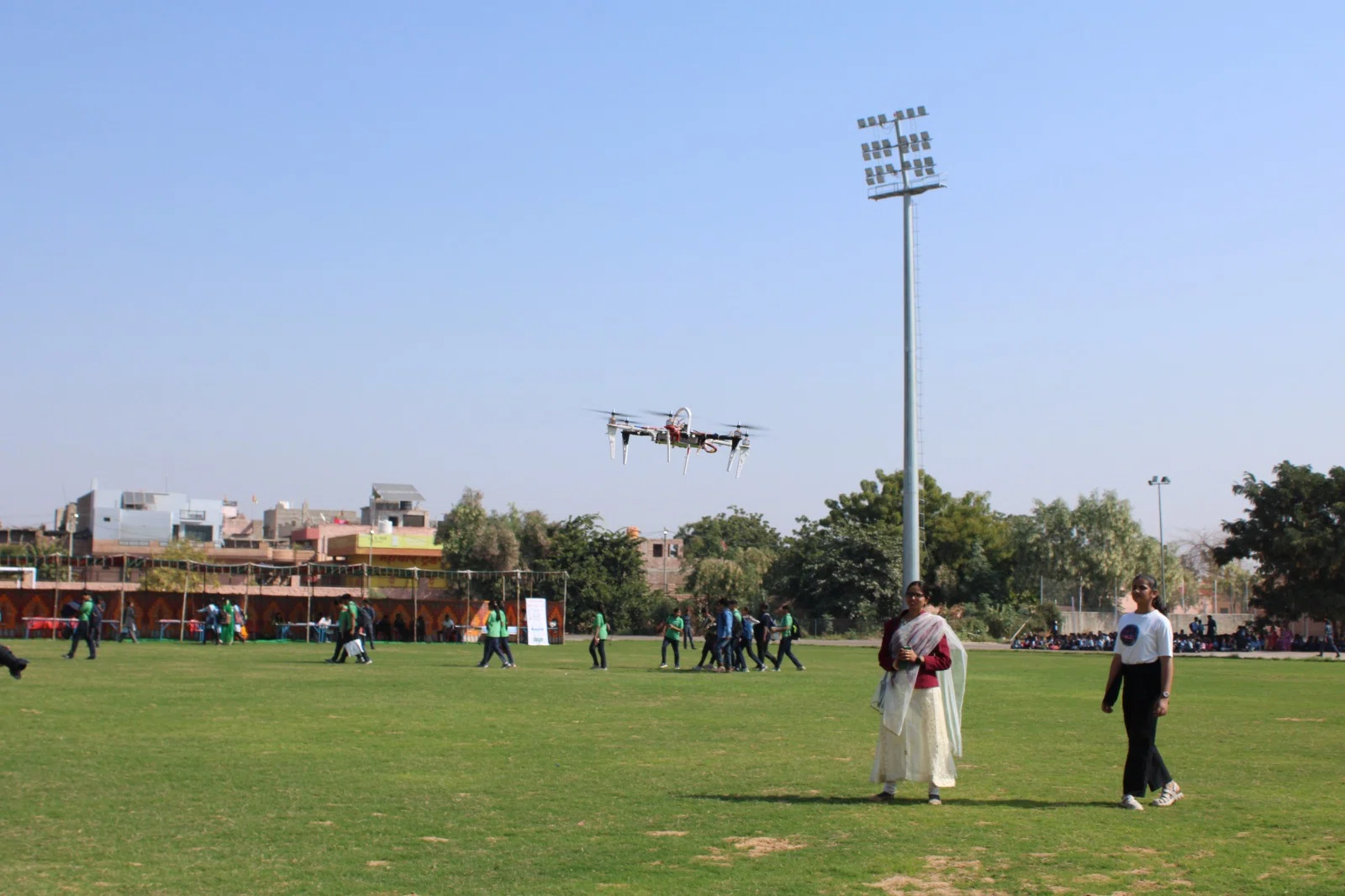 A model aircraft flying above students on the fair grounds